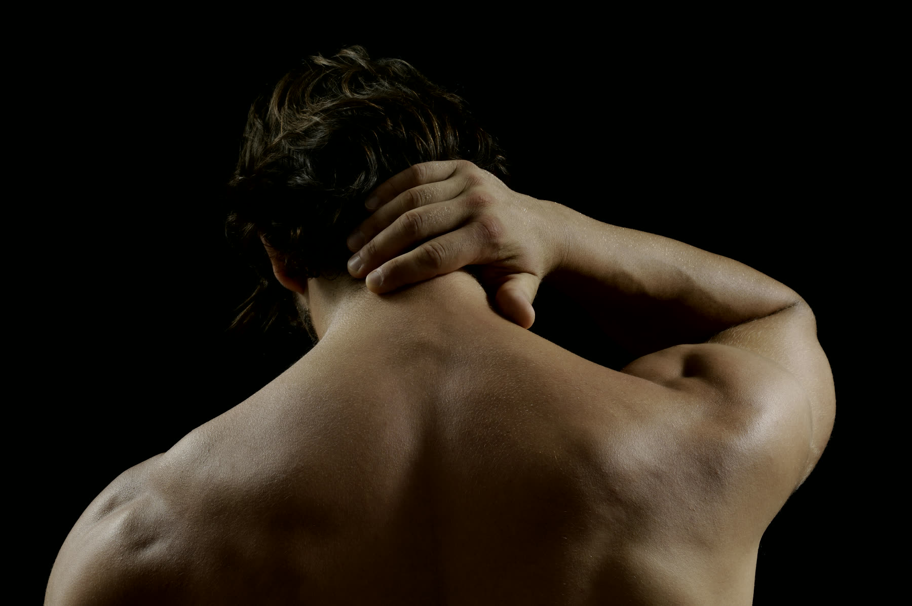 A man seen from behind, holding the back of his neck
