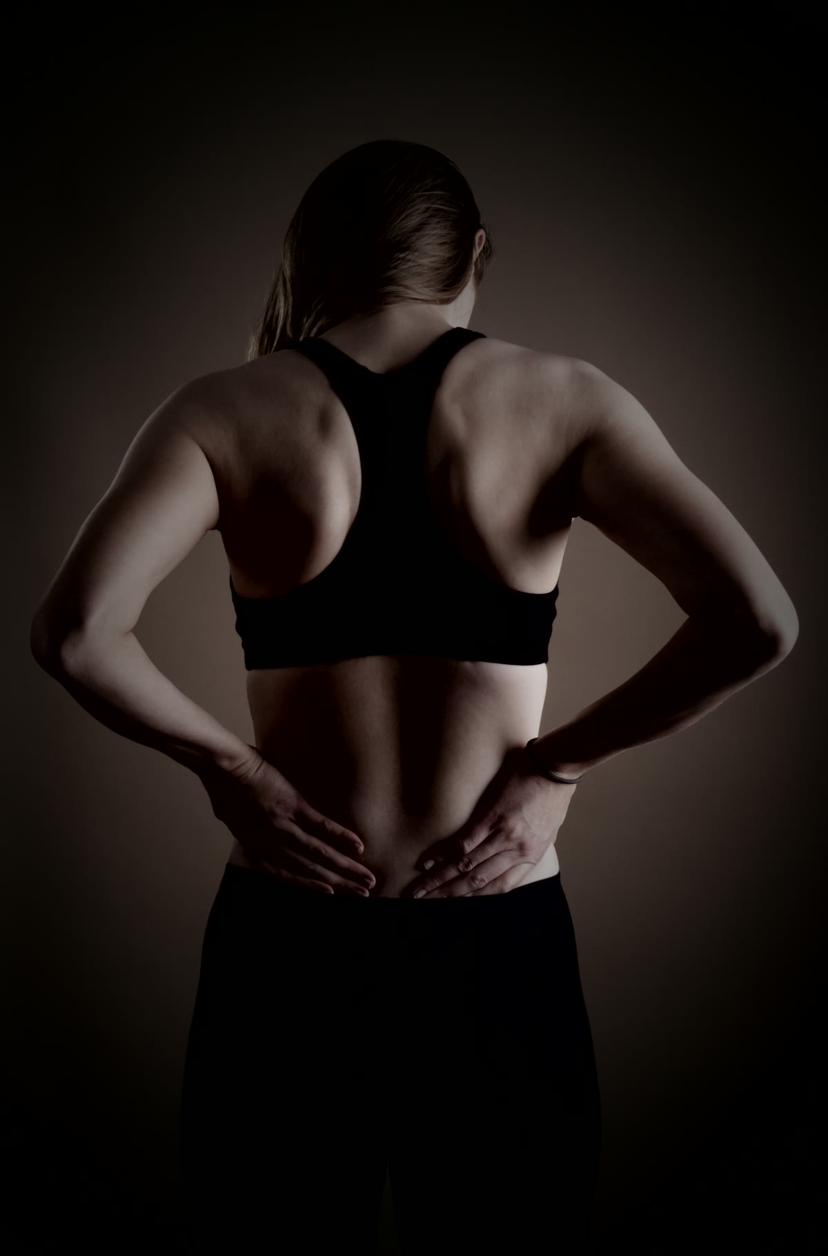 A person seen from behind with both hands pressed to the base of the spine